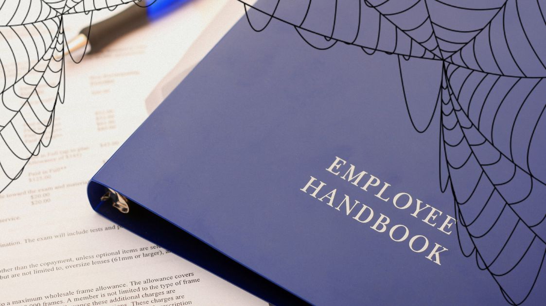 Employee handbook covered in spiderwebs, symbolizing outdated workplace policies and the need for an updated handbook.